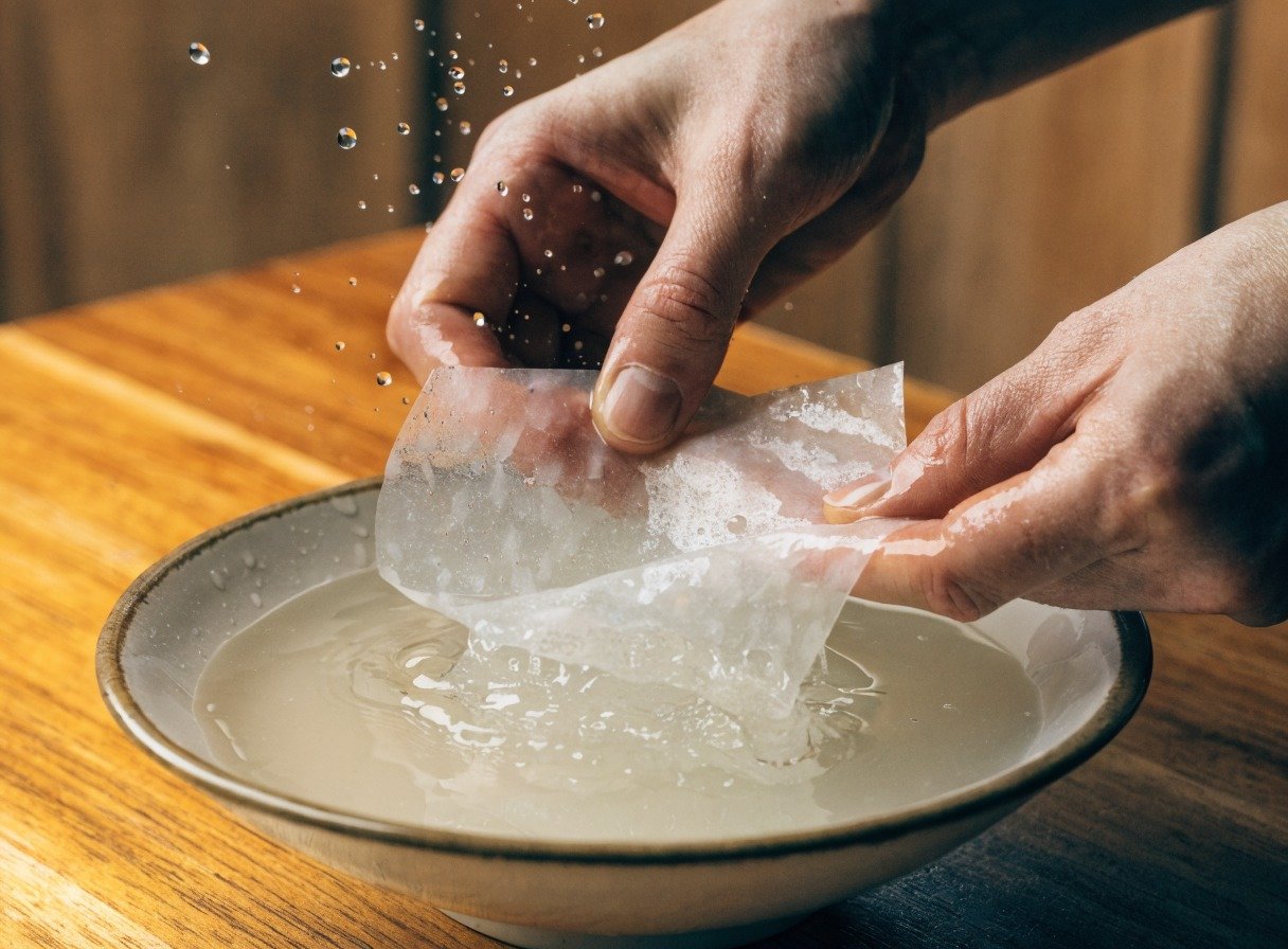 What is the best filling for rice paper dumplings? cooking process - Action shot of hands dipping a translucent sheet of rice paper into a shallow bowl of lukewarm water