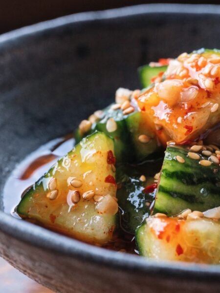 Why do you smash cucumbers in a salad? - Stunning photorealistic hero shot of smashed cucumber salad in a dark ceramic bowl, glistening with chili oil, garlic bi