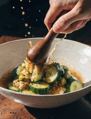 Why do you smash cucumbers in a salad? - Stunning photorealistic hero shot of Why do you smash cucumbers in a salad with garlic and sesame dressing in a ceramic