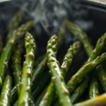 How long does frozen asparagus take to cook in an air fryer? recipe hero presentation - A close-up photorealistic shot of vibrant green asparagus spears cooking inside a black air fryer ba